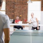Man and woman in office space playing ping pong